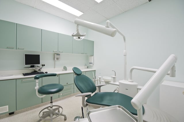 dental office with chair, with a desktop computer behind it, white walls