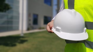 contractor with a holographic jacket holding a white hard hat