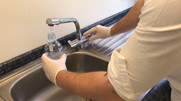 man with white gloves doing a Legionella test in a sink